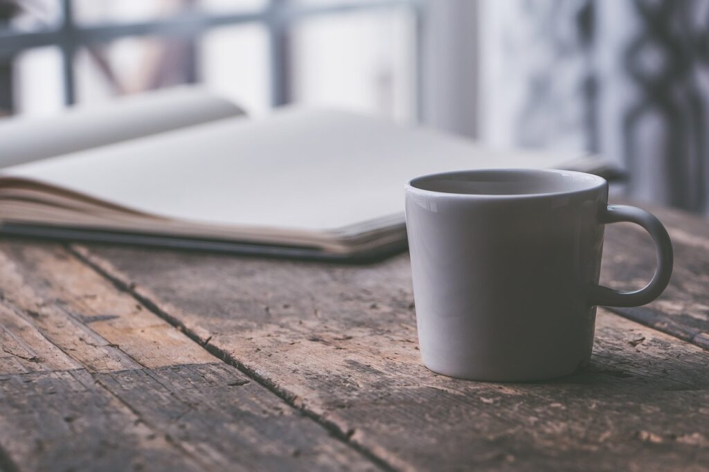 A mug with coffee inside next to a mental health journal with the pages open